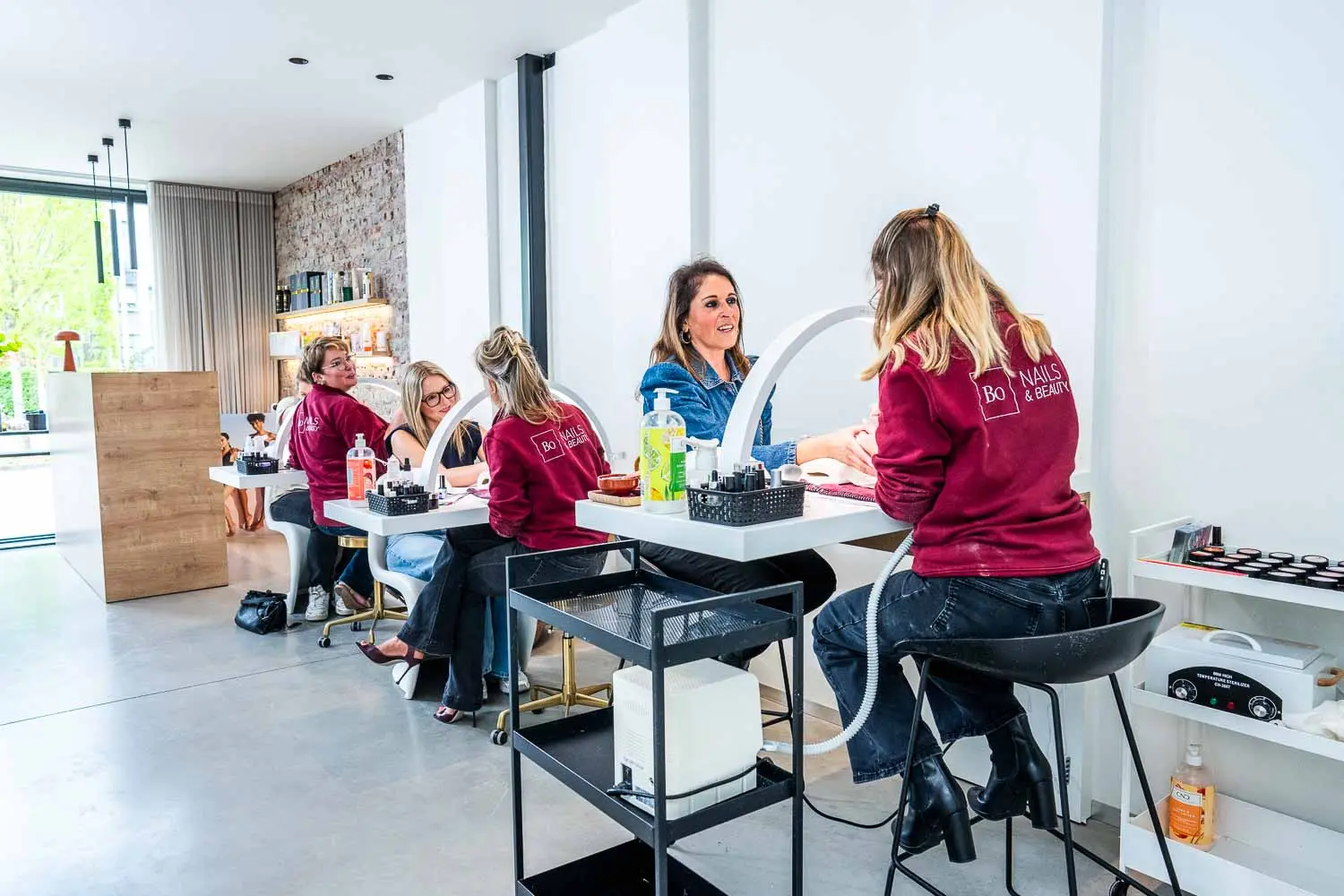 Team van nagelstylistes aan het werk bij Bo-Nails & Beauty in Merelbeke – overzicht van de moderne nagelstudio met meerdere manicureplekken en tevreden klanten.