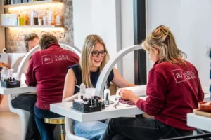 Professionele manicurebehandeling bij nagelstudio Bo-Nails & Beauty Gent-Merelbeke – een lachende klant geniet van persoonlijke nagelverzorging door het deskundige team.